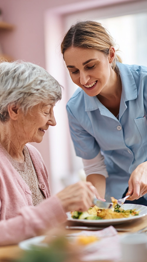 Accompagnante éducative et sociale aidant une personne âgée pendant le repas
