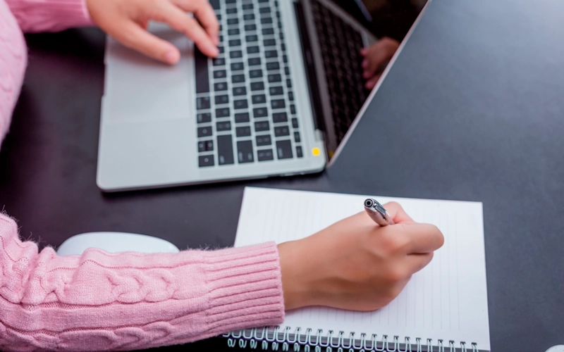 Femme prenant des notes à son bureau devant son ordinateur